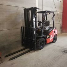 Una carretilla elevadora roja y negra está estacionada en un almacén.