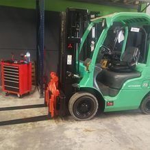 Una carretilla elevadora verde está estacionada en un garaje al lado de una caja de herramientas roja.