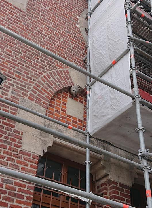 Façade d'un bâtiment en briques avec une fenêtre cintrée, des échafaudages et un nid de guêpes.