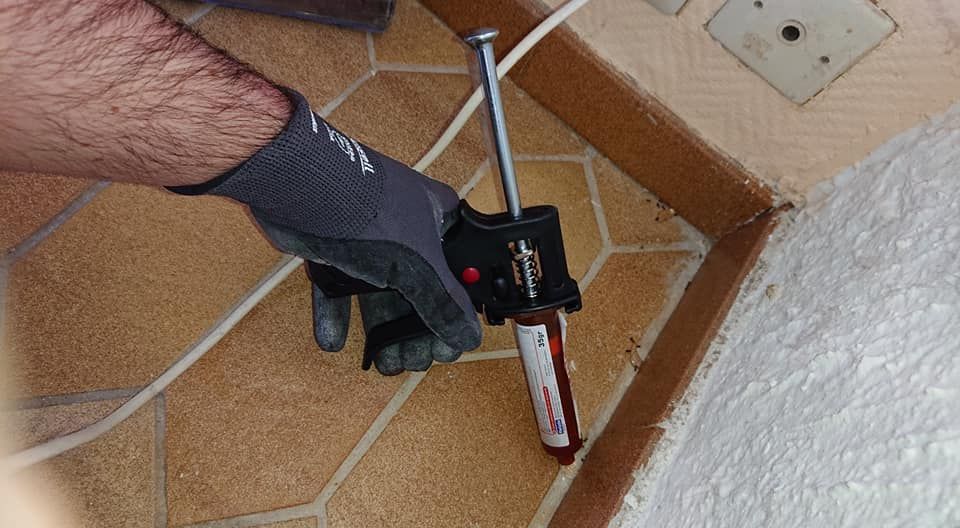 Main gantée utilisant un pistolet à calfeutrer sur une surface carrelée près d'un coin.