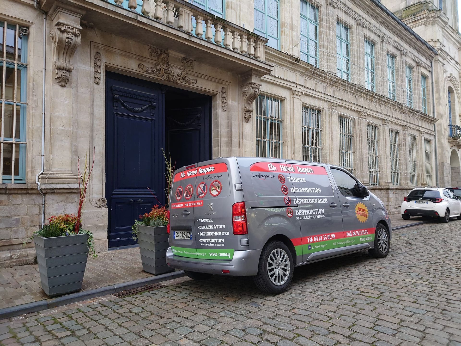 Camionnette garée devant un immeuble à la façade ornée et aux portes bleues ouvertes.