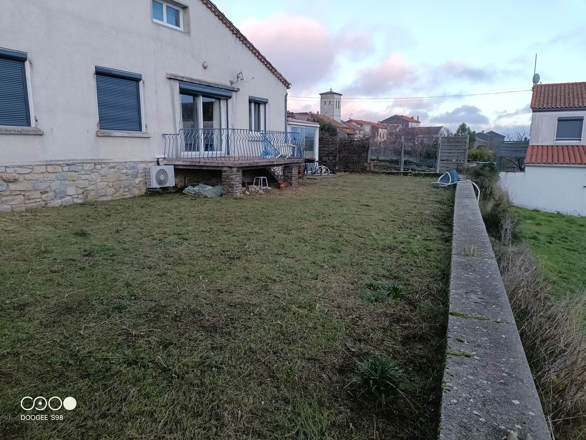 Une maison avec une cour, un mur de pierre et un ciel couvert.