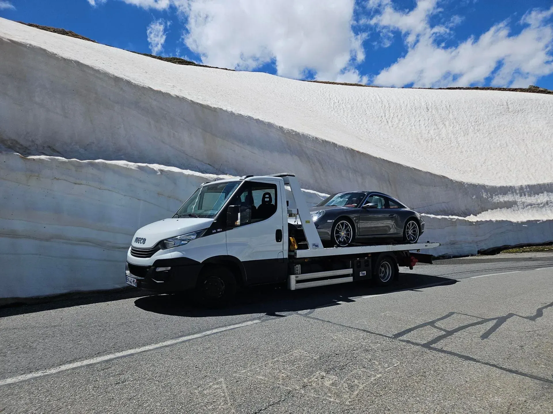 Voiture équipée de pneus neige sur une route enneigée dans un paysage montagneux.