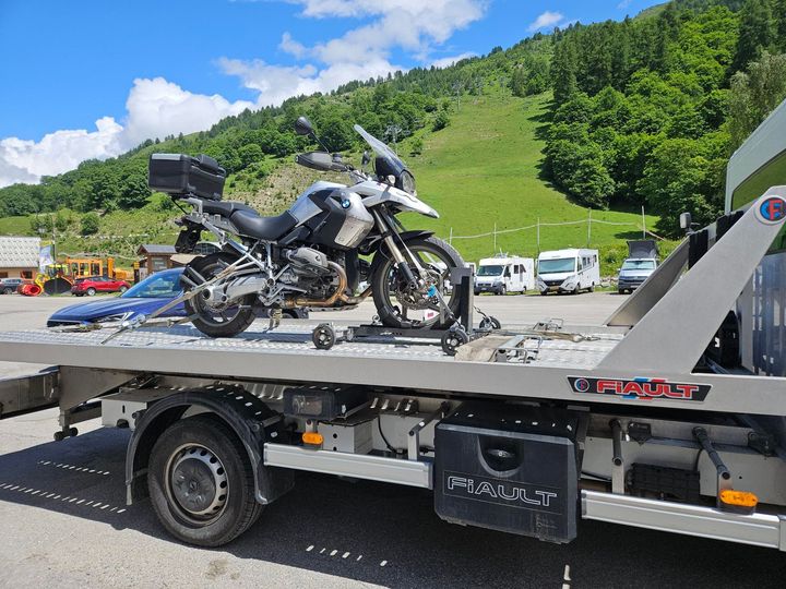 Moto sur une dépanneuse à plateau, en extérieur, près des montagnes et d'autres véhicules.