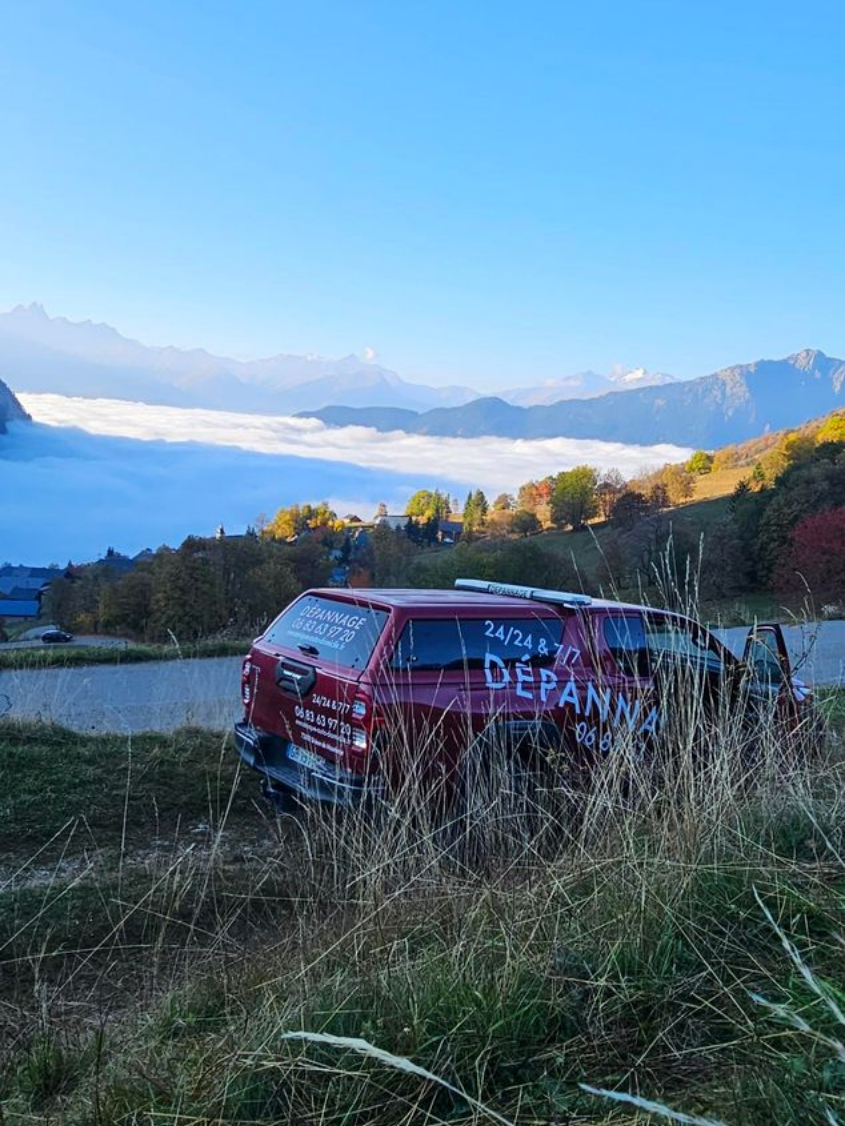 Triangle de signalisation devant une voiture en panne sur la route, une personne se tient à proximité.