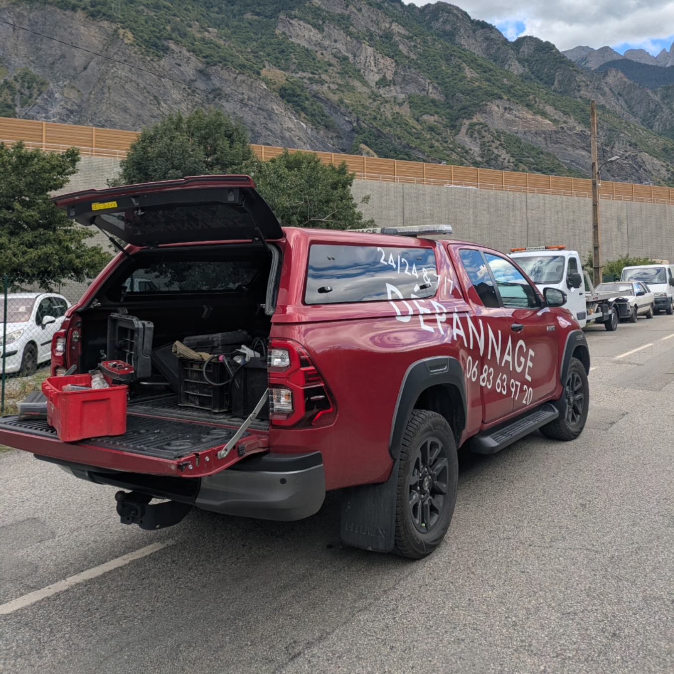 Camionnette rouge à hayon ouvert, stationnée sur la route ; montagnes en arrière-plan.