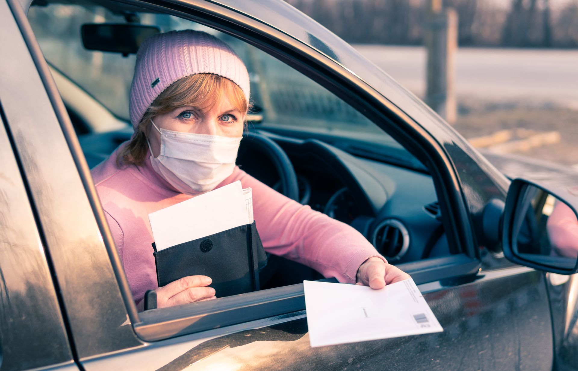 Une femme portant un bonnet et un masque tendant une prescription de transport par la fenêtre