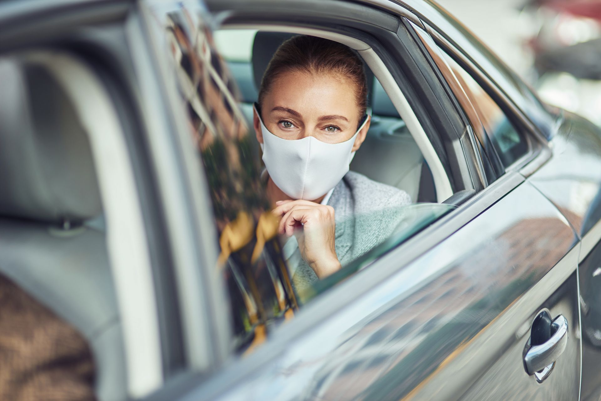 Une femme qui porte un masque à l'arrière d'une voiture avec la vitre ouverte