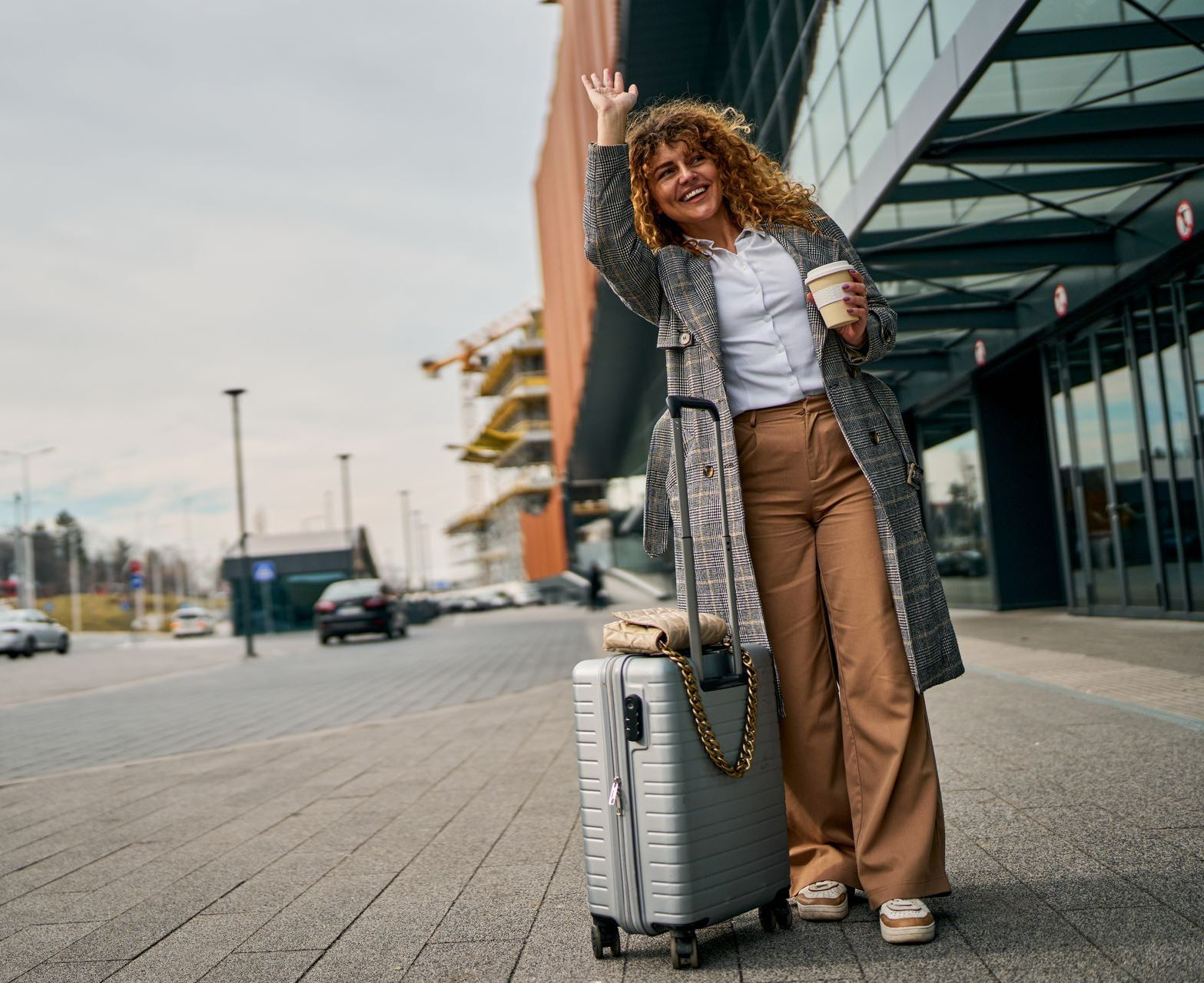 Une femme avec un gobelet de café à la main levant la main pour appeler un taxi
