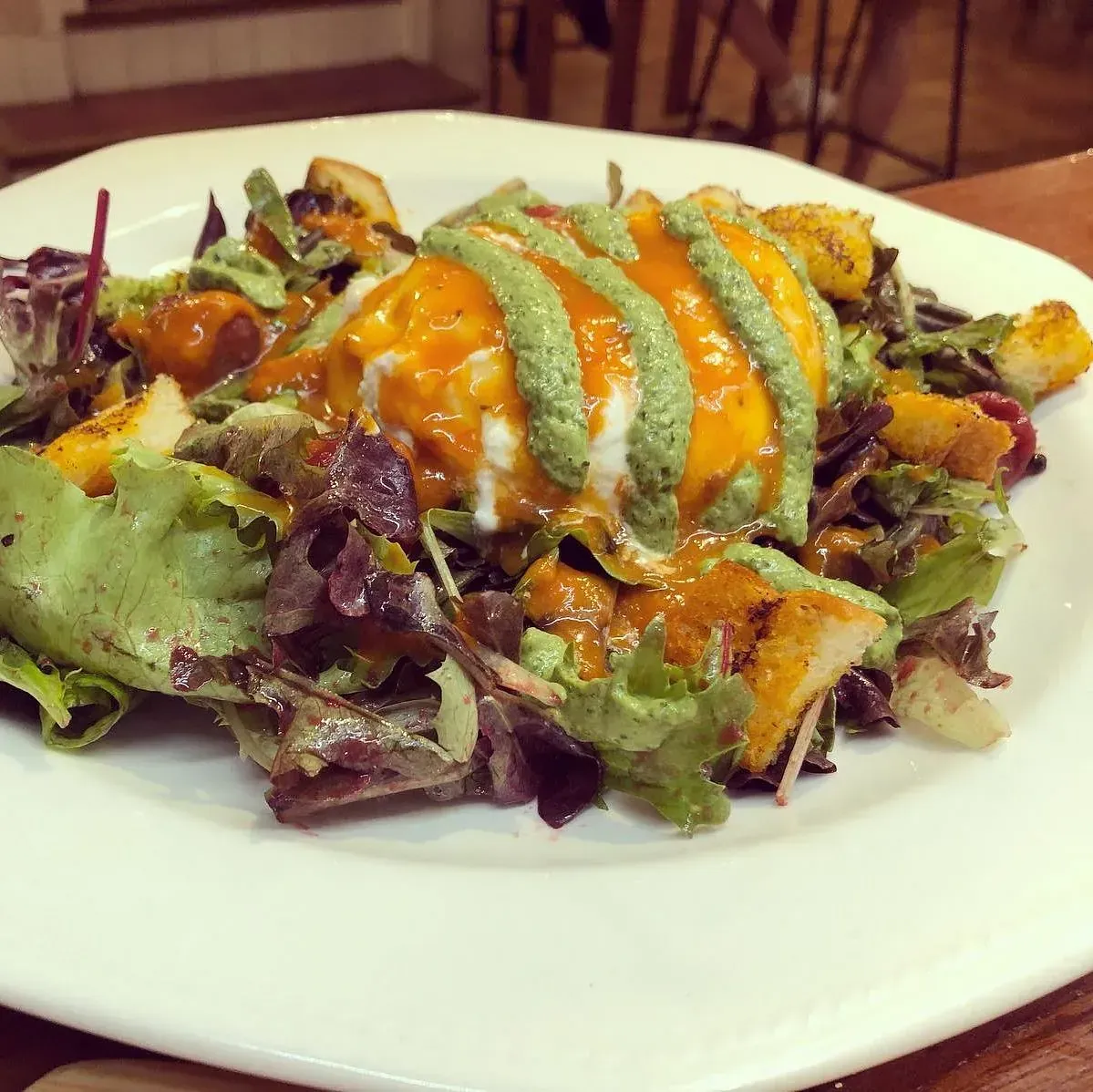 Ensalada con huevo escalfado, aderezada con salsas de naranja y verde, en un plato blanco.