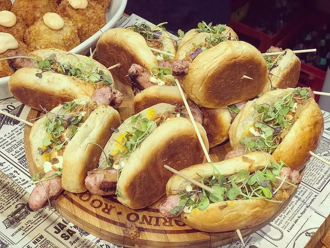 Perros calientes sobre tabla de madera, cubiertos con verduras.