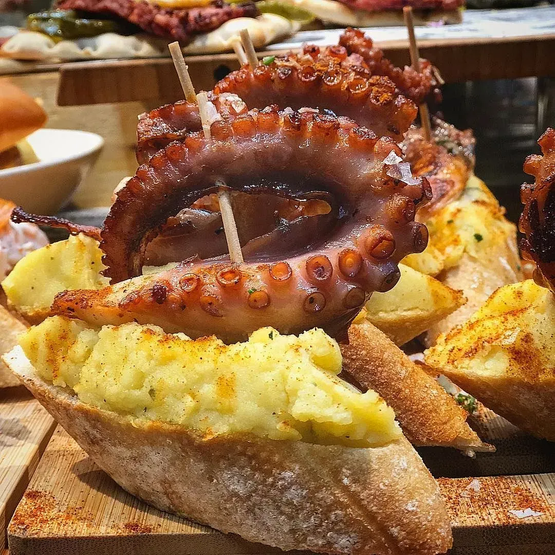 Pulpo a la plancha sobre pan con puré de patatas, tabla de madera para servir.