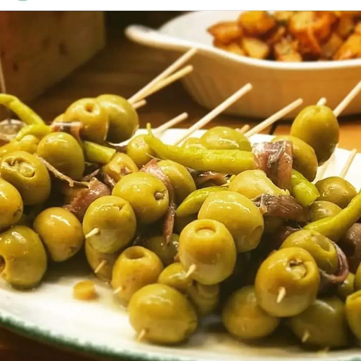 Aceitunas verdes, pimientos y anchoas en brochetas servidas en un plato blanco.