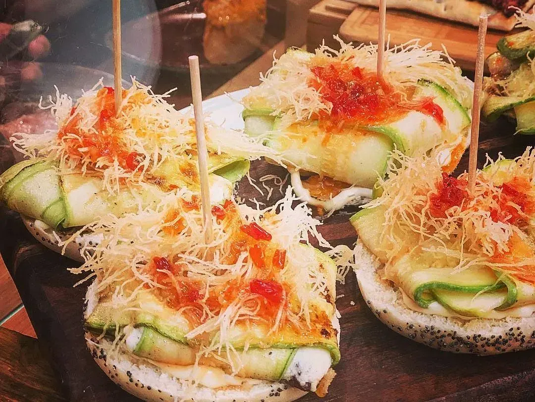 Sándwiches abiertos con calabacín, queso y salsa roja, sujetos con palillos, sobre una tabla de madera.