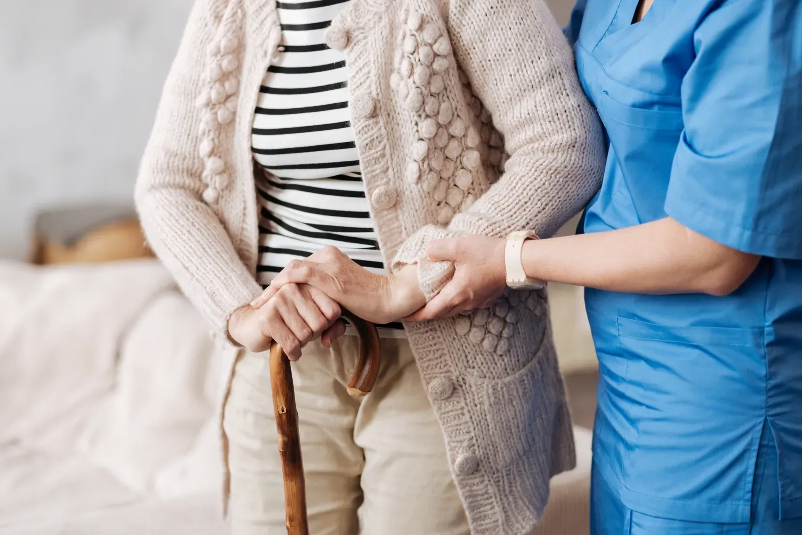 Eine Krankenschwester hilft einer älteren Frau mit einem Gehstock.