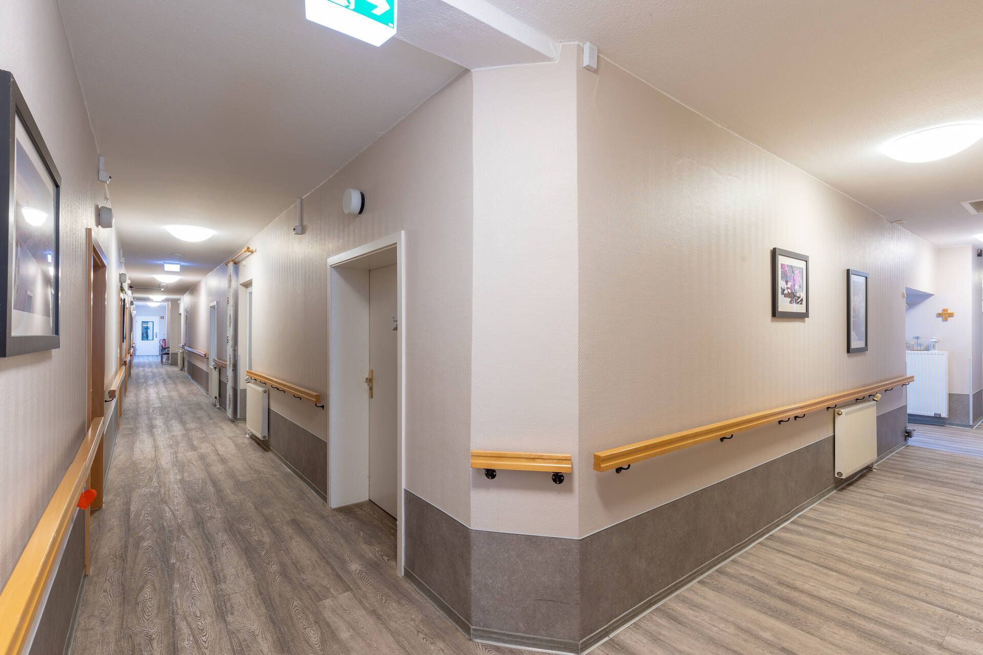 Ein langer Flur in einem Altenwohn- und Pflegeheim mit Holzhandläufen an den Wänden.