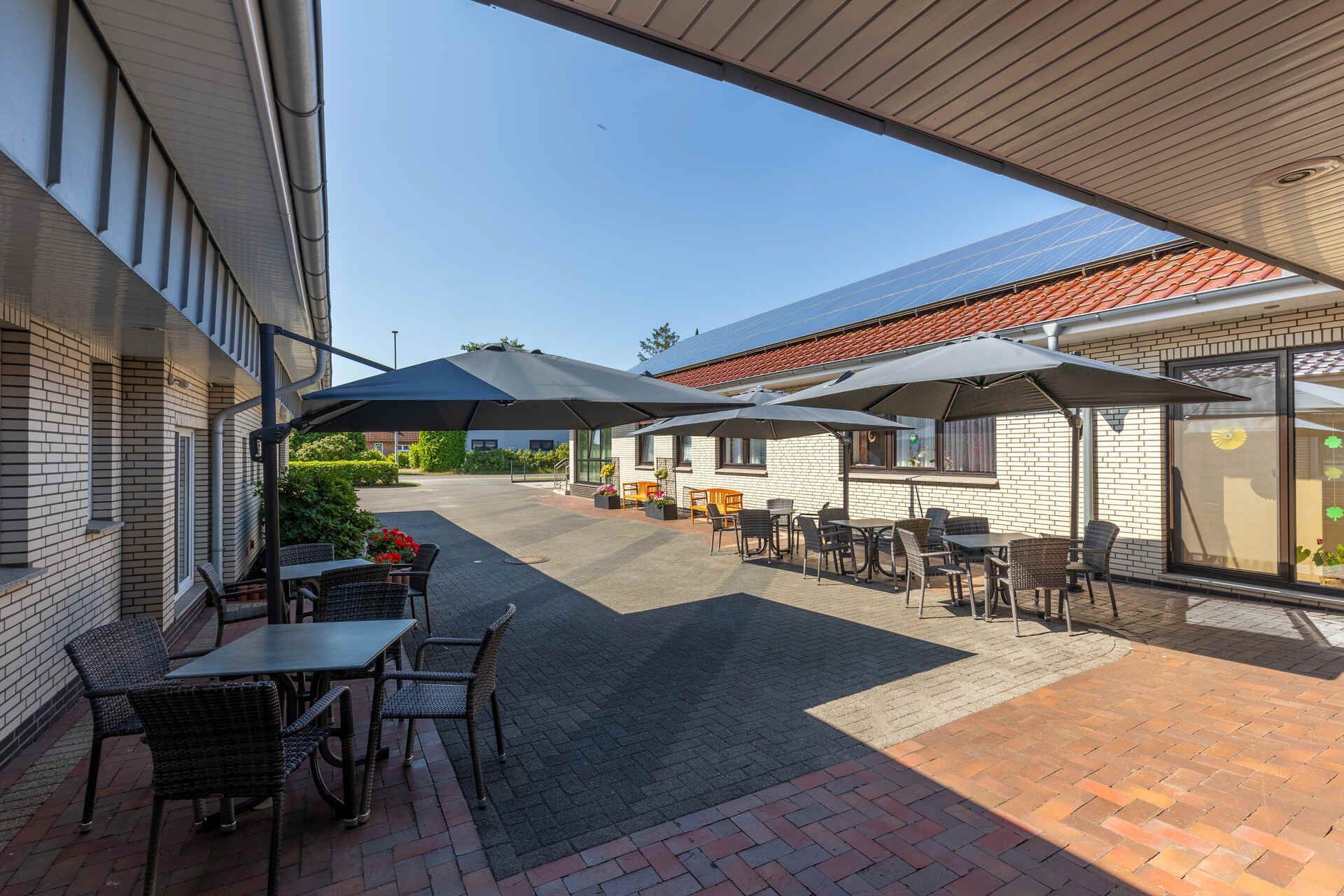 Ein Hof mit Tischen, Stühlen und Sonnenschirmen vor einem Altenwohn- und Pflegeheim.