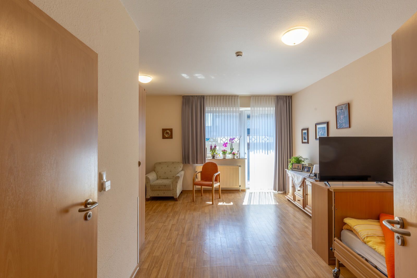 Ein Wohnzimmer mit Bett, Sessel, Fernseher und Balkon.