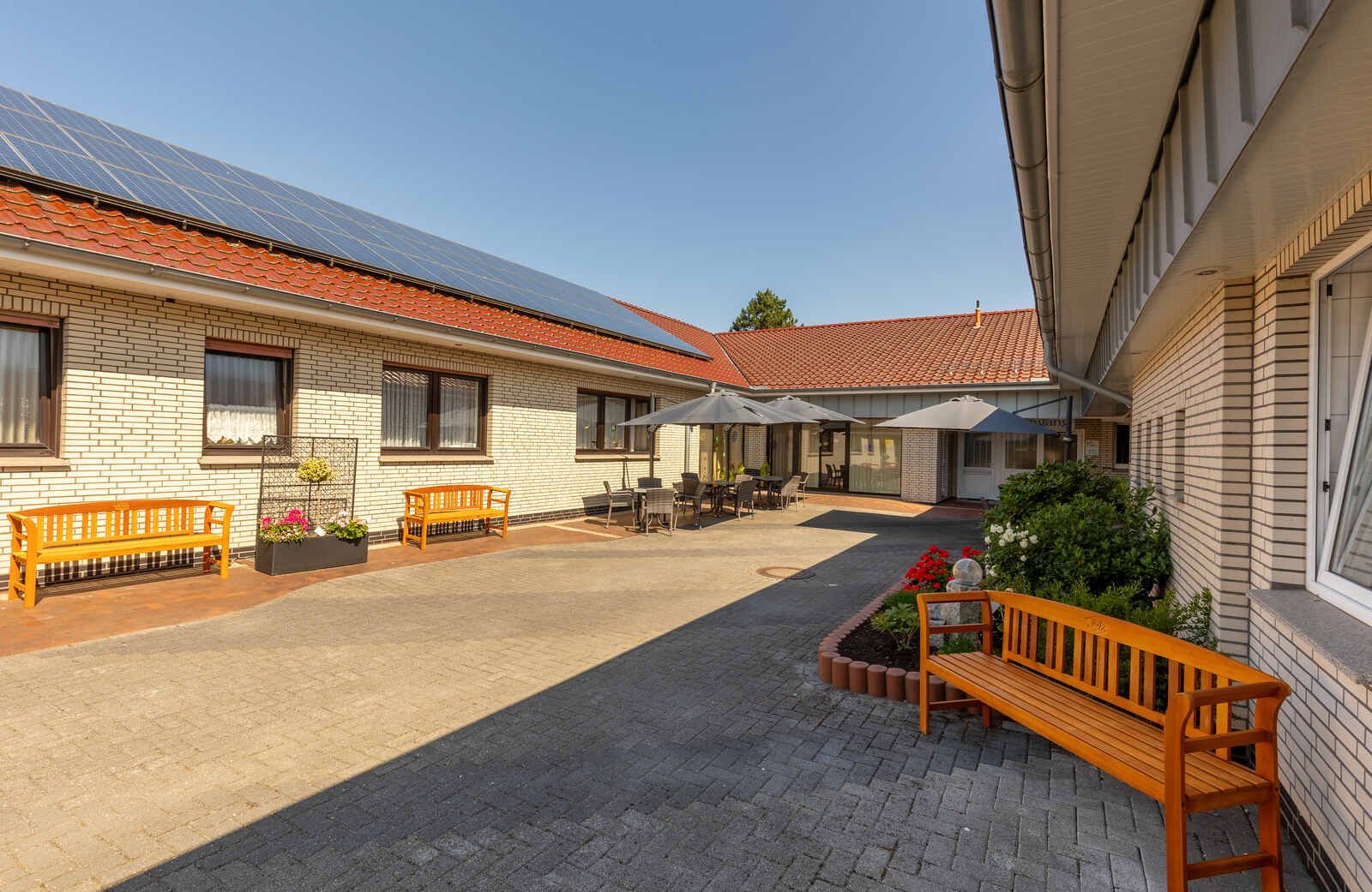 Eine Holzbank steht in der Mitte eines Hofes zwischen zwei Gebäuden.