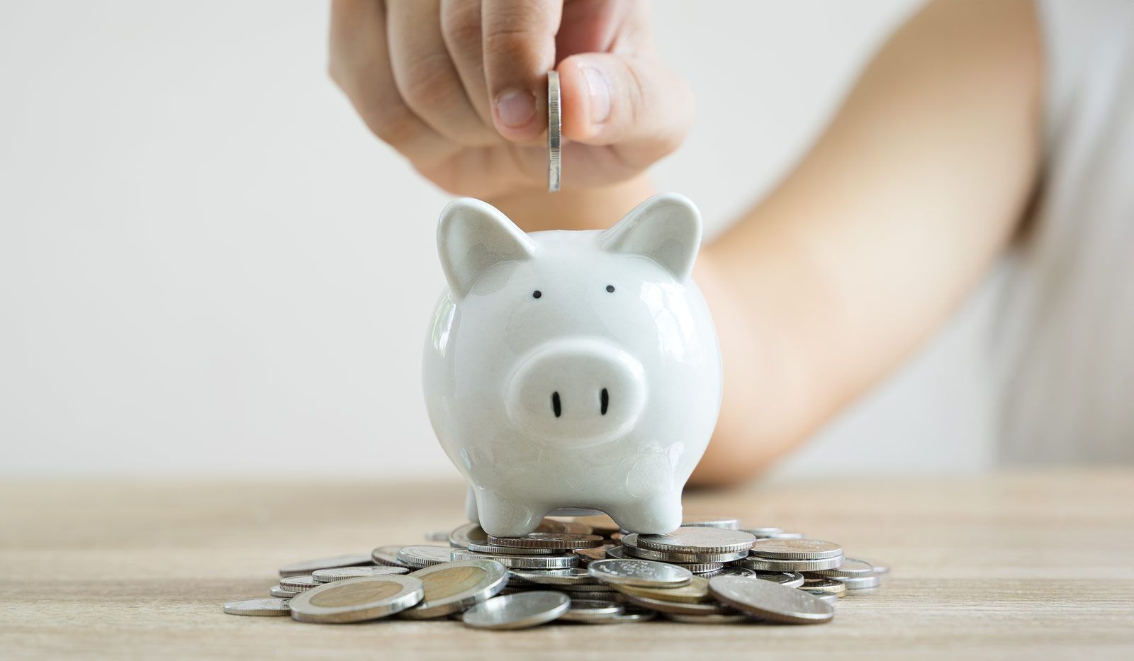 Eine Person wirft eine Münze in ein Sparschwein.
