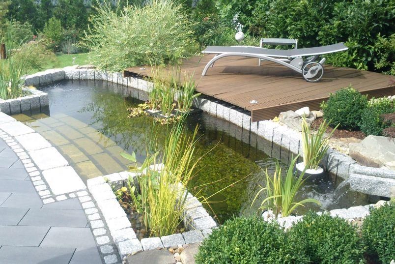 Ein Gartenstuhl steht auf einer Terrasse mit Blick auf einen Teich