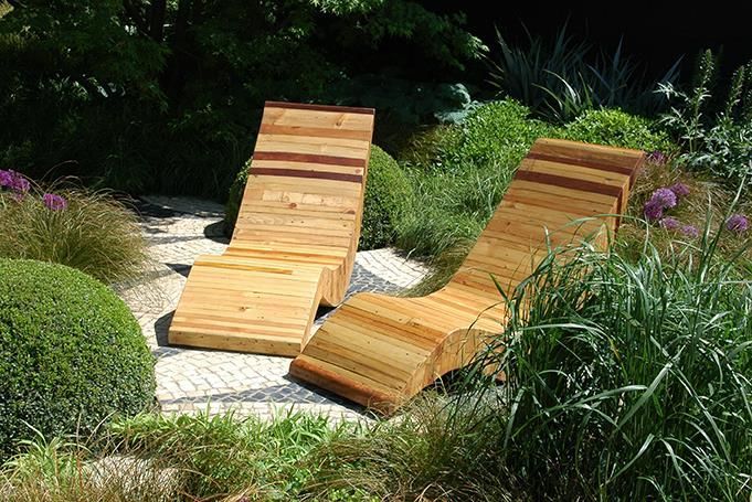 Zwei hölzerne Liegestühle in einem Garten mit lila Blumen