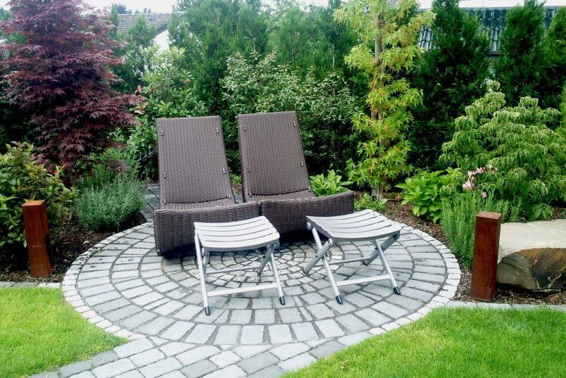 Eine Terrasse mit zwei Stühlen und Ottomanen in einem Garten