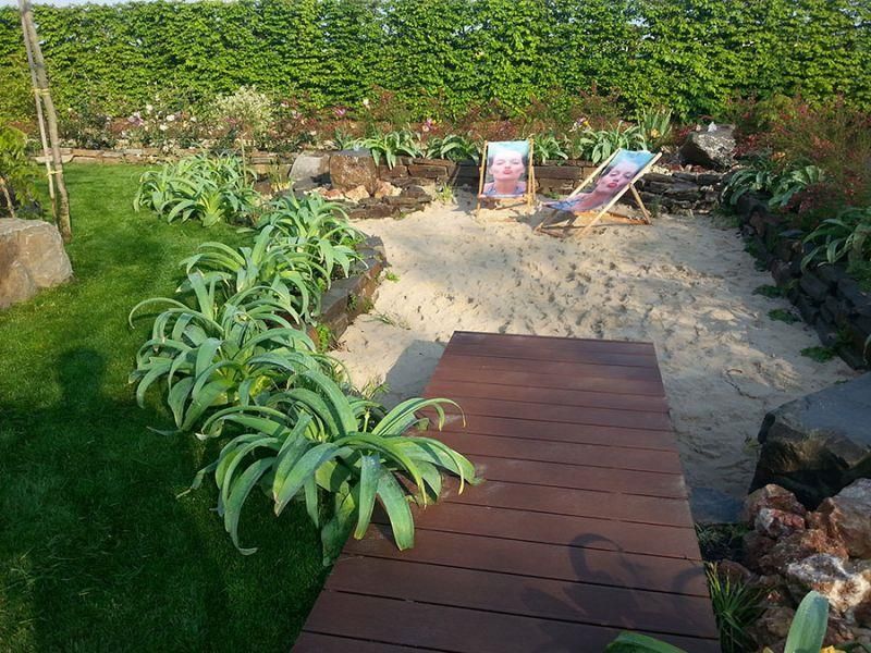 Ein Holzsteg führt zu einem Sandbereich mit Liegestühlen