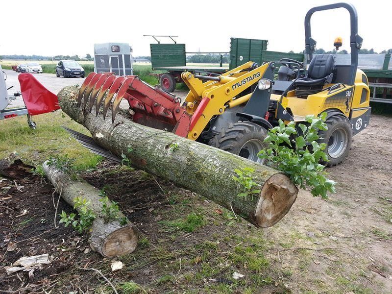 Ein gelber Traktor schneidet einen großen Baumstamm in den Dreck