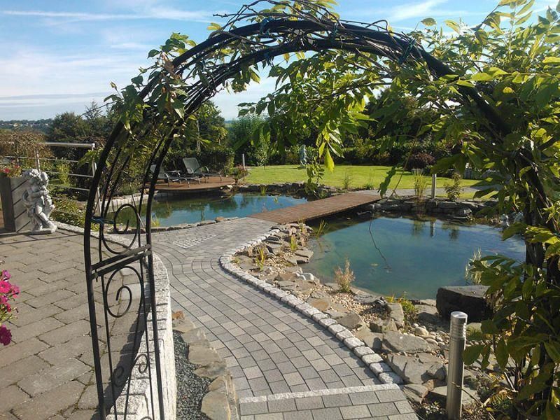 Ein Weg, der zu einem Teich mit einem schmiedeeisernen Torbogen führt