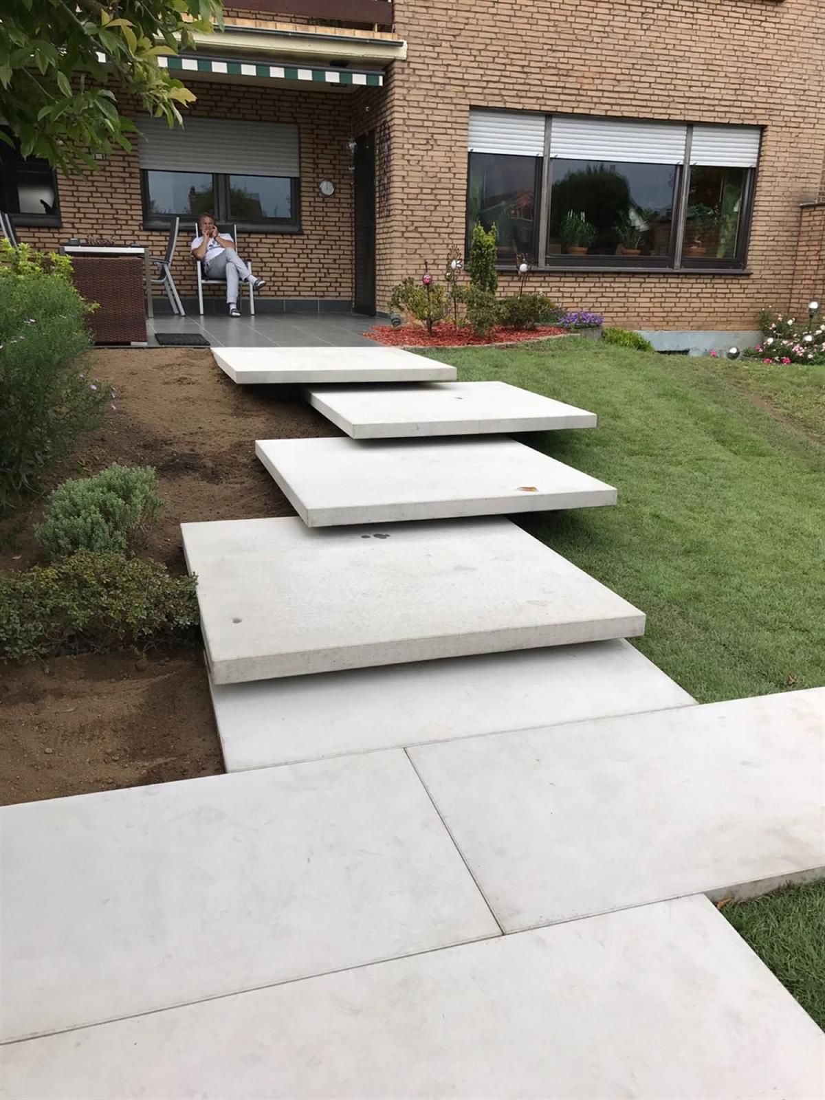 Eine Frau sitzt auf einem Stuhl auf einer Terrasse vor einem Haus.