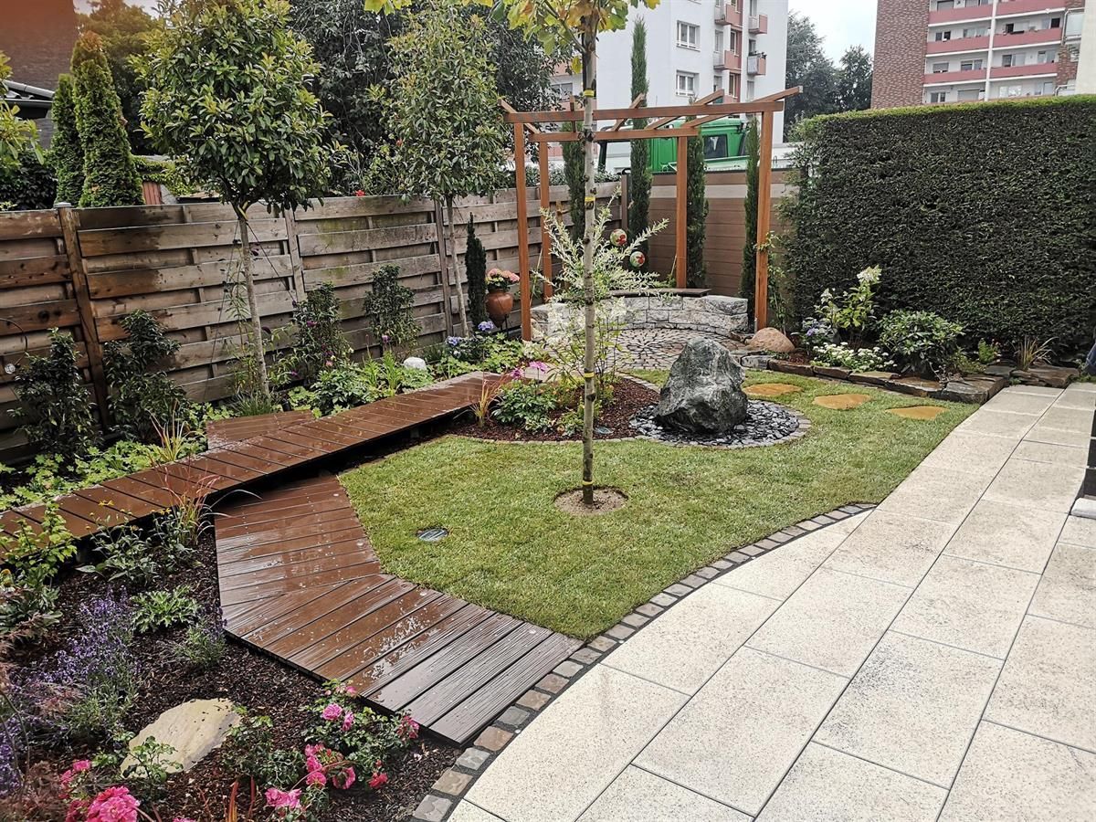 Ein üppiger grüner Garten mit einer Holzbrücke und einem Ziegelweg