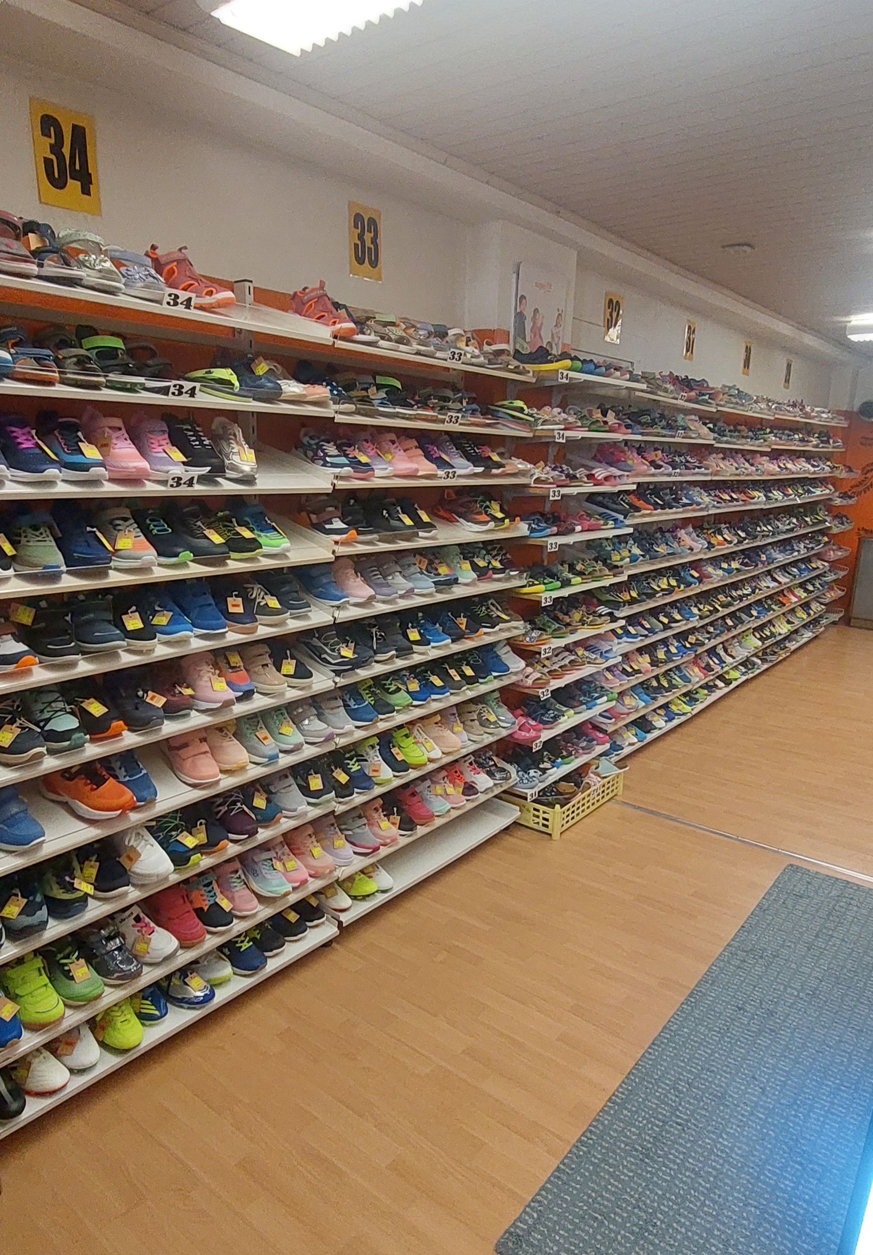 Gang in einem Schuhgeschäft mit Reihen von Sportschuhen, die auf Holzregalen ausgestellt sind.