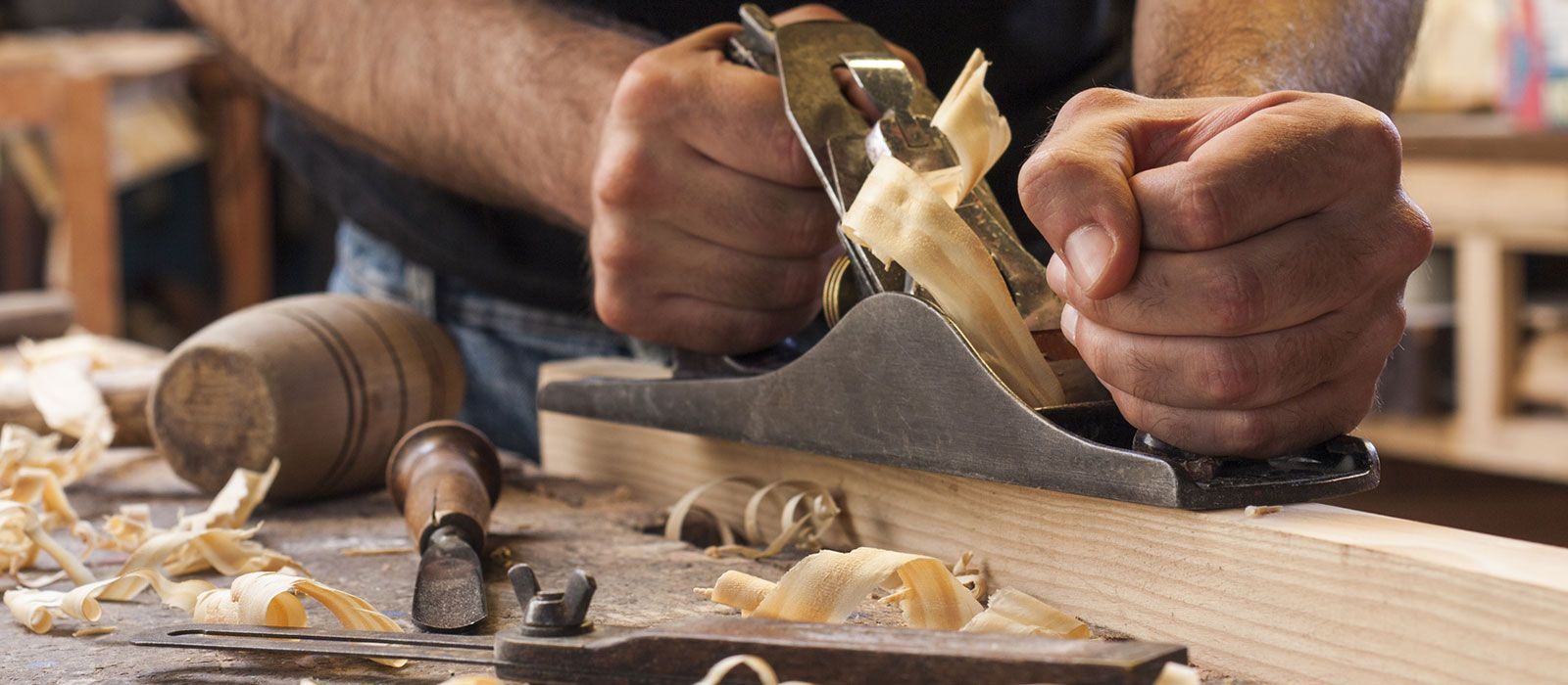Ein Mann hobelt mit einem Hobel ein Stück Holz