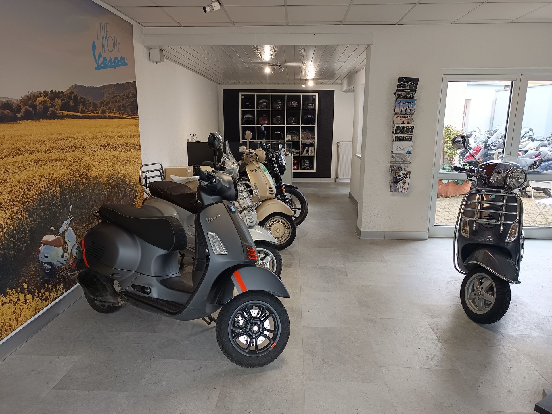 Roller im Ausstellungsraum: Graue, beige und schwarze Vespa-Modelle werden drinnen präsentiert.