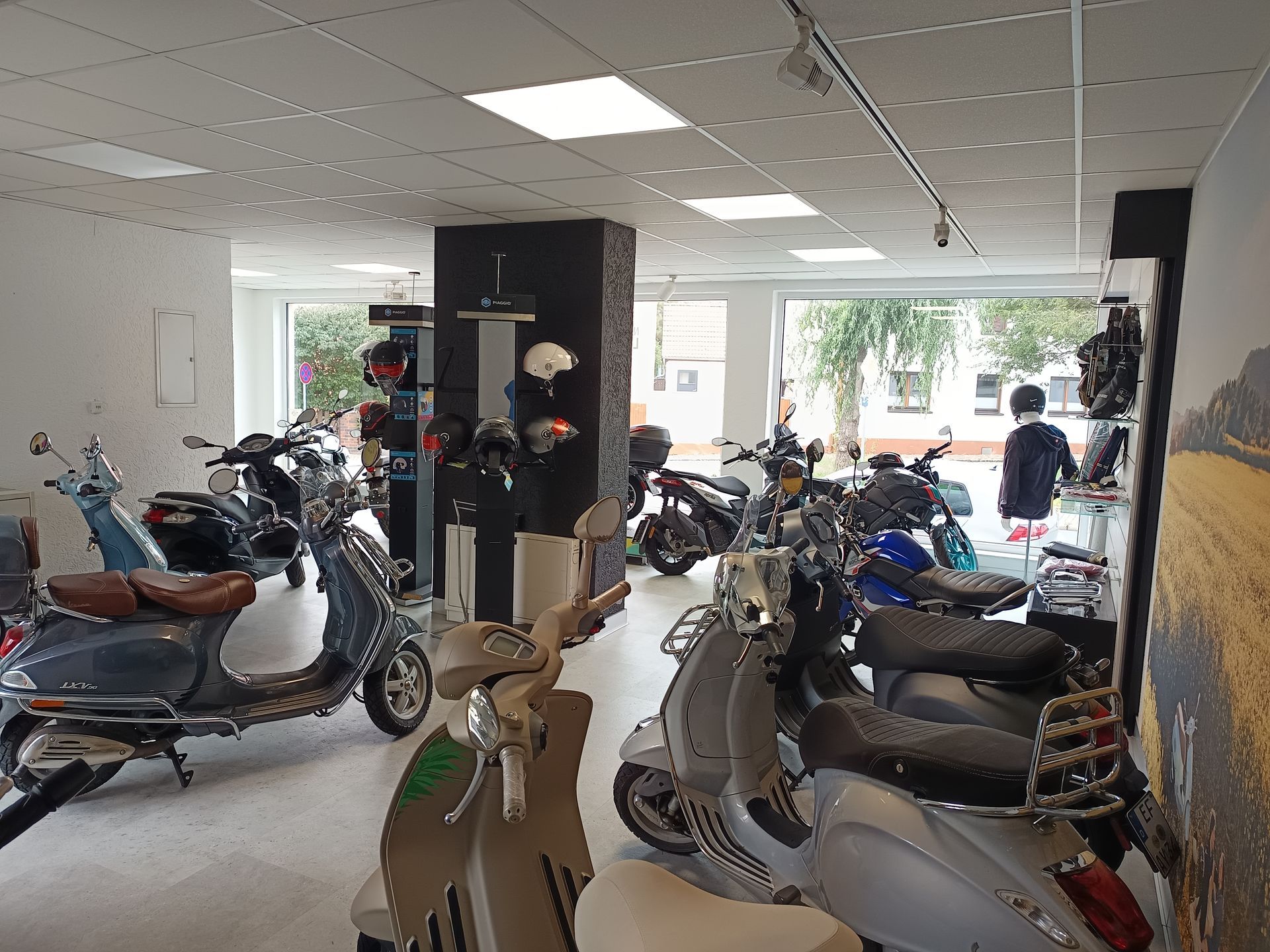 Innenansicht eines Roller-Showrooms mit verschiedenen ausgestellten Modellen. Eine Person schaut sich in der Nähe des Schaufensters um.