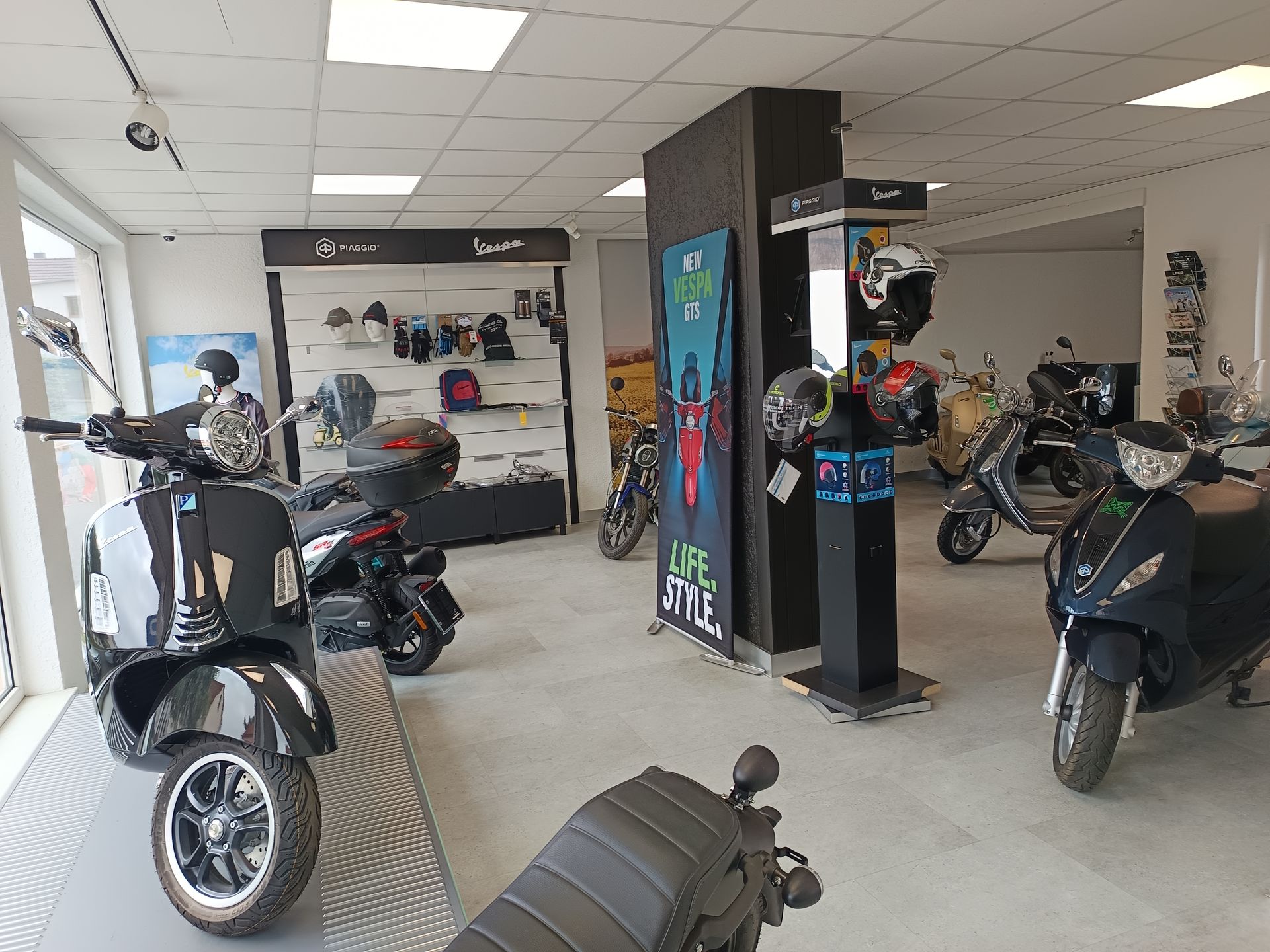 Innenansicht eines Rollerladens mit mehreren geparkten Rollern, Helmen und ausgestelltem Zubehör.
