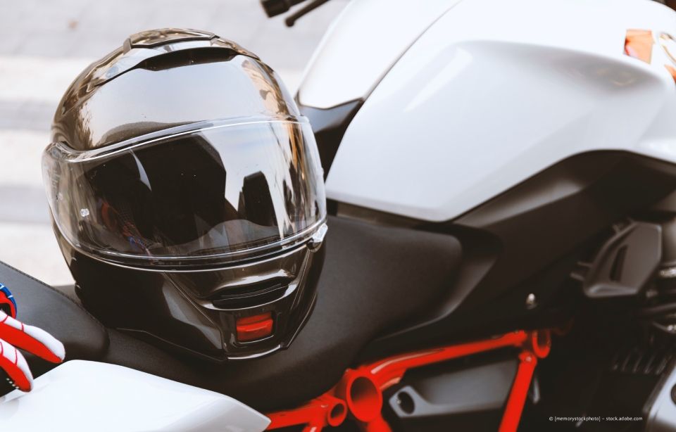 Schwarzer Motorradhelm auf einem weißen Motorradsitz mit roten Akzenten.