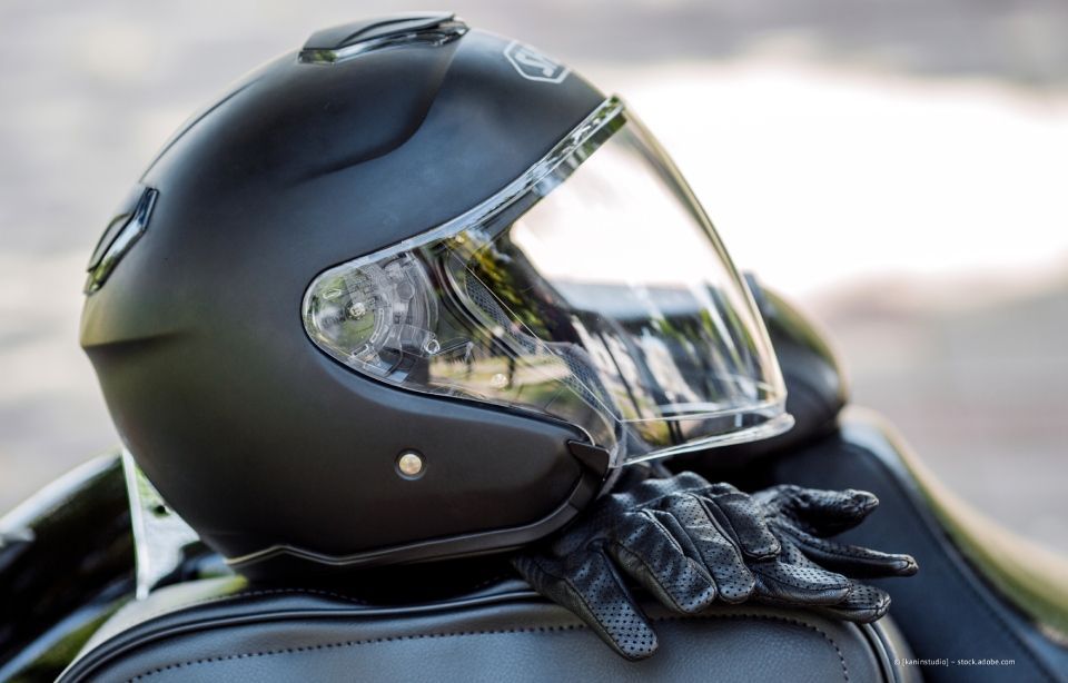 Schwarzer Motorradhelm mit klarem Visier und schwarze Handschuhe auf einem Motorradsitz.