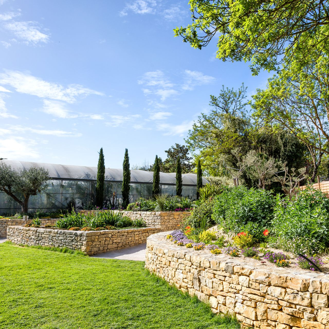 Des murets en pierre délimitent différents parterres d'un jardin.