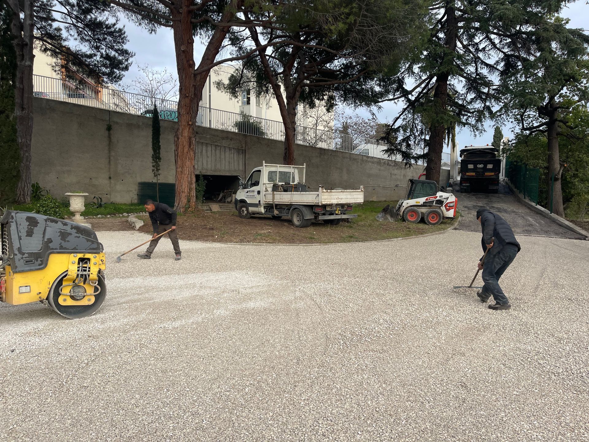 Des ouvriers étalent du gravier dans une cour.