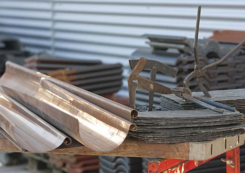 Eine Kupferrinne liegt auf einem Holztisch neben einer Zange