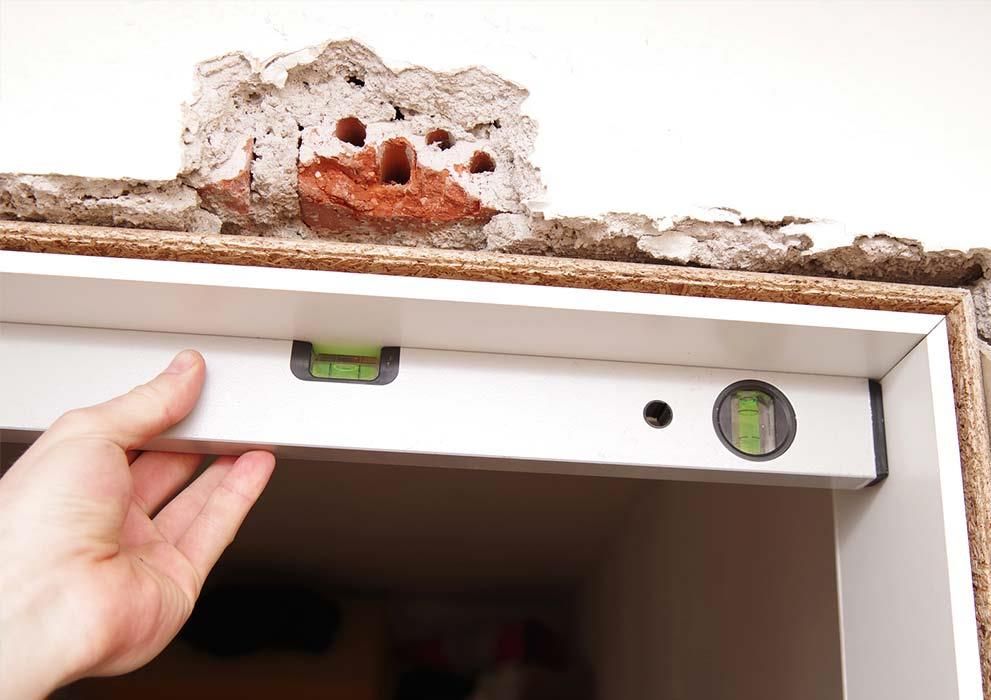 Eine Person überprüft mit einer Wasserwaage die Höhe eines Türrahmens