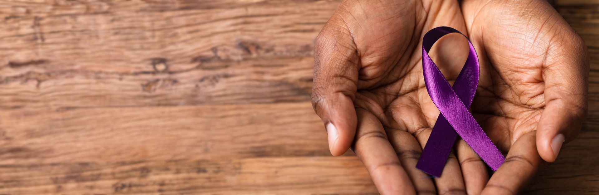 Mains jointes tenant un ruban violet sur fond de bois