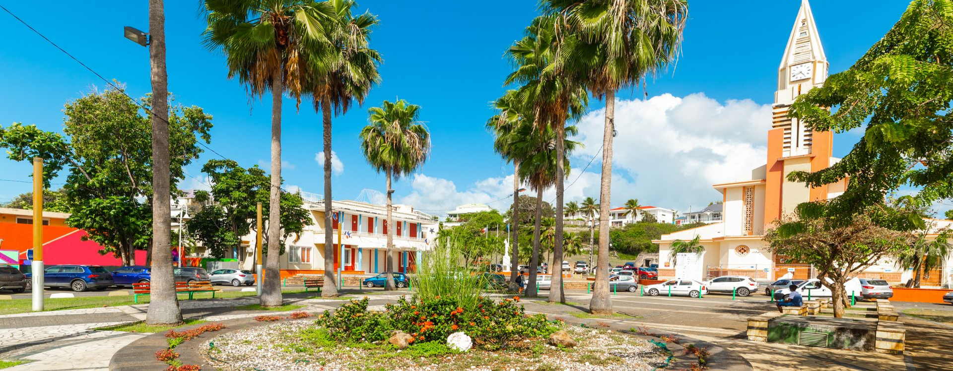 Une place ensoleillée bordée de grands palmiers, de bâtiments colorés et d'une église