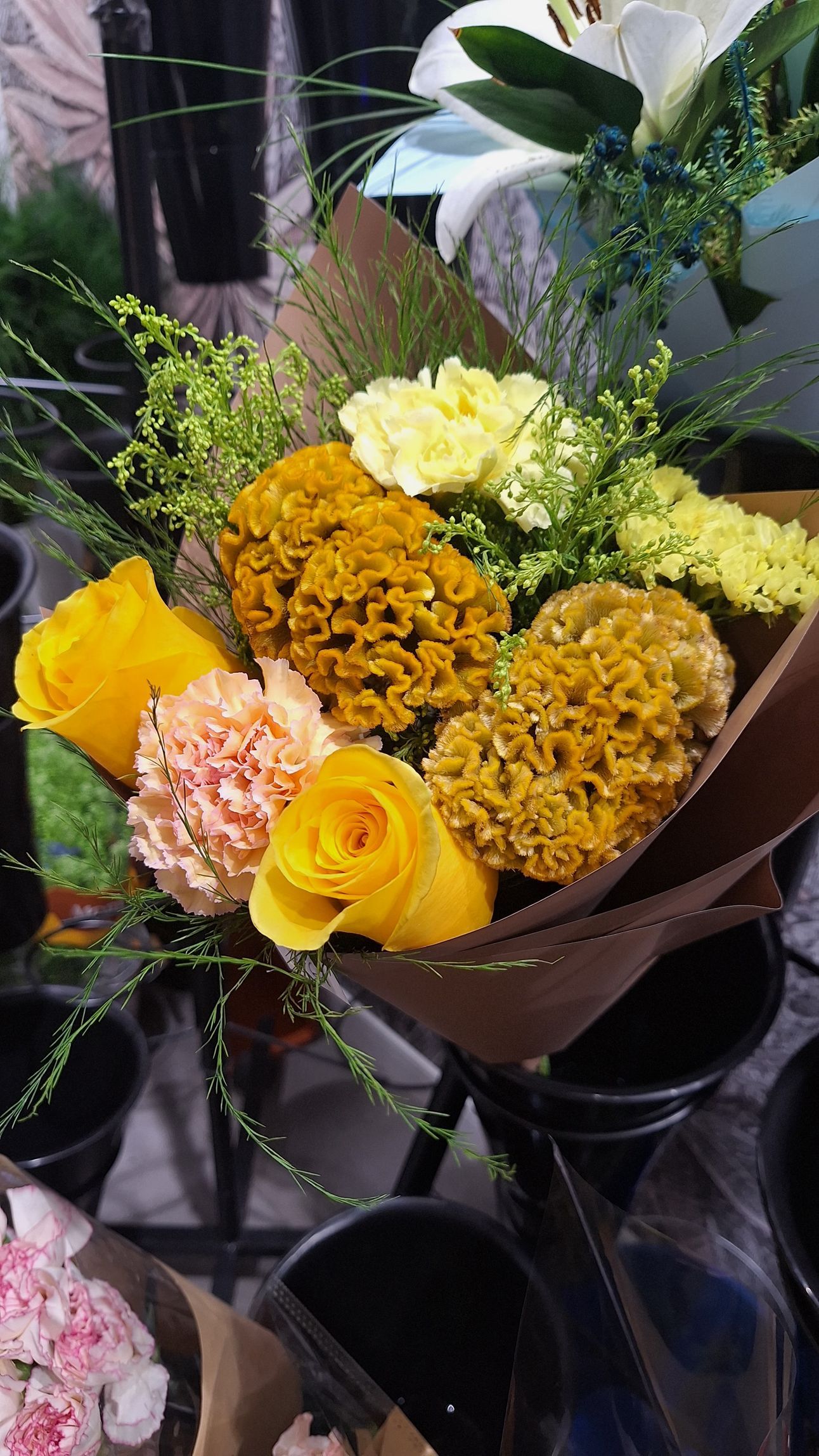 Ramo de flores amarillas, blancas, rosas y naranjas envuelto en papel oscuro.