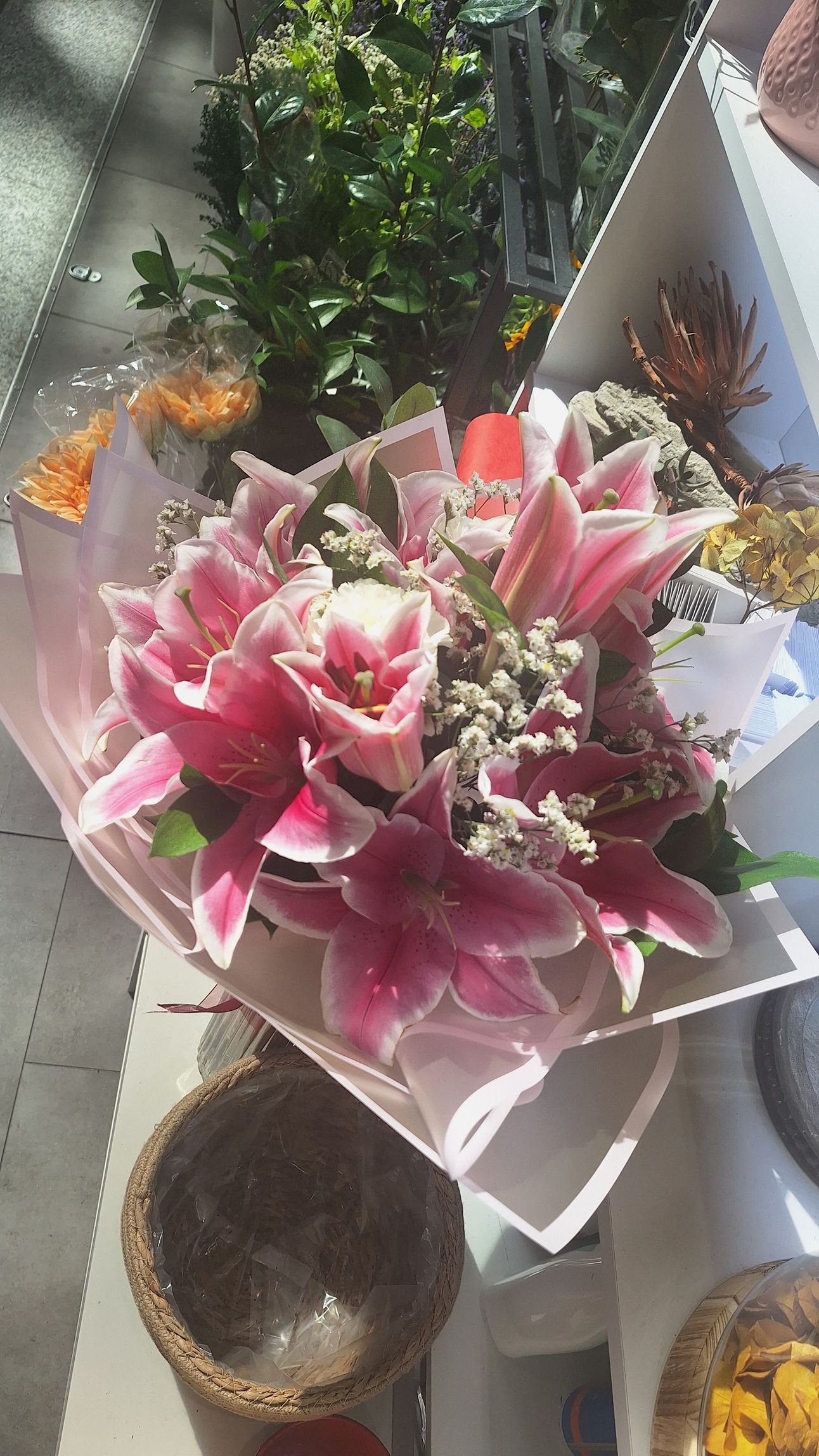 Lirios rosas y blancos en un ramo junto a una ventana con plantas en macetas cerca.