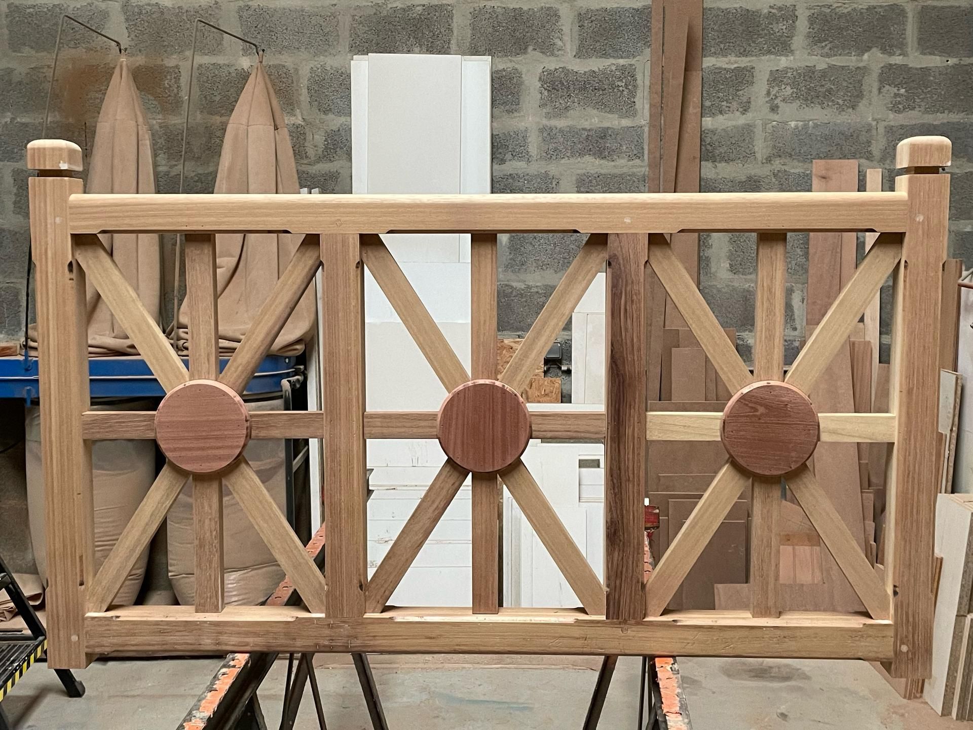 Un panneau de rambarde en bois partiellement assemblé, orné de centres décoratifs circulaires, posé sur des établis dans un atelier.