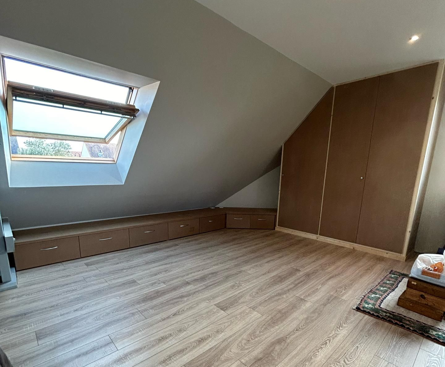 Une chambre mansardée avec plafond en pente, parquet clair, rangements intégrés en bois discrets et hautes armoires.