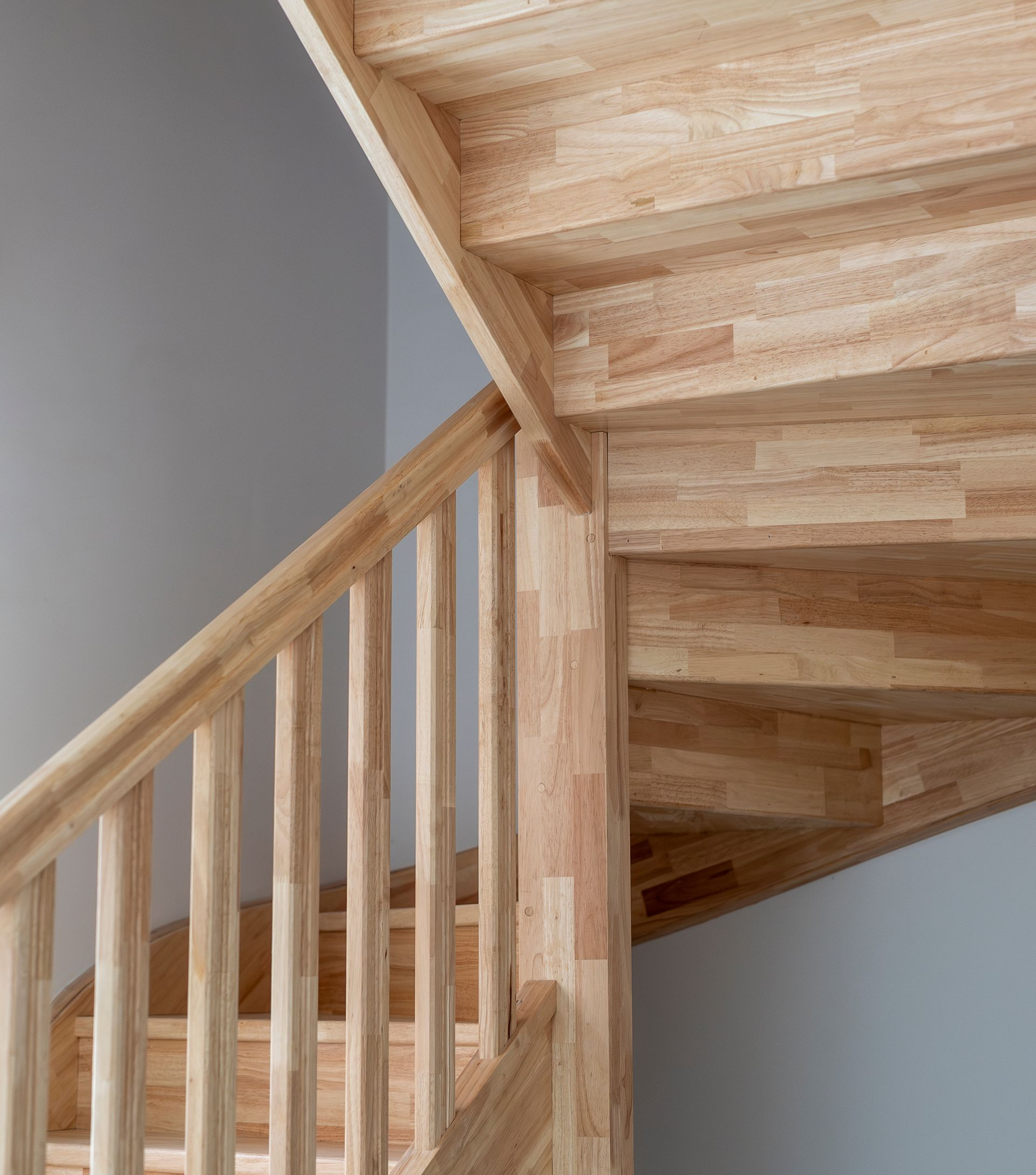 Un escalier en bois clair, avec une rampe assortie, serpente vers le haut contre un mur gris clair uni.